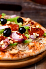 Pizza with chorizo ​​sausage, mozzarella cheese, green pepper and black olives. Rustic wooden background. Soft focus.	