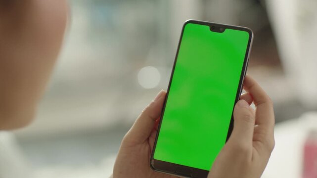 Smartphone user looking green screen display at office desk close up. Unrecognizable businessman hand holding chroma key cellphone at work break. Manager checking email on mobile phone at morning.