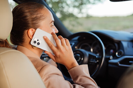 A focused woman holds a smartphone to her ear, talking on a call while driving.