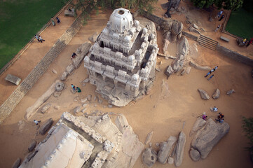 Mahabalipuram, India - 17 September 2006: Aerial view of the monolithic rock-cut architecture of Pancha Rathas, bathed in warm sunlight, casting long shadows on the sandy landscape.