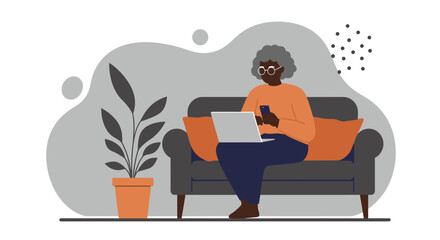 Elderly African American woman comfortably using a laptop and smartphone on a sofa at home, showcasing modern senior engagement with technology and connectivity.
