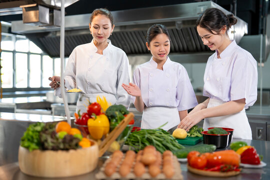 Professional chef teaching young culinary class student to prepare fresh ingredient for the meal inside the restaurant kitchen for fine dining gourmet and cooking school