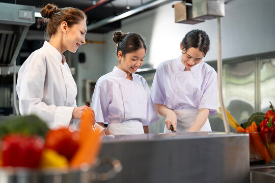 Professional chef is teaching young culinary class student to prepare fresh ingredient for the meal inside the restaurant kitchen for fine dining gourmet and cooking school