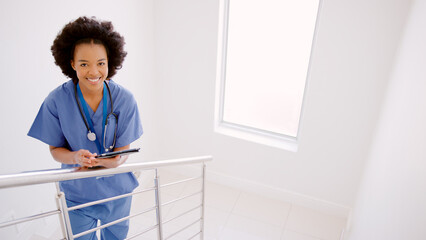 Portrait Of Female Doctor Or Nurse With Digital Tablet Checking Patient Notes On Stairs In Hospital