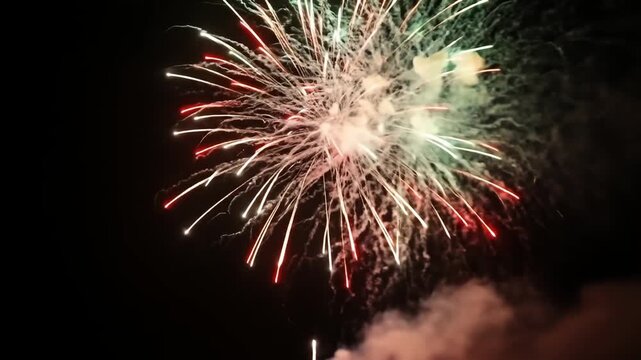 Burst of fireworks exploding against black background with green, white, & red hues