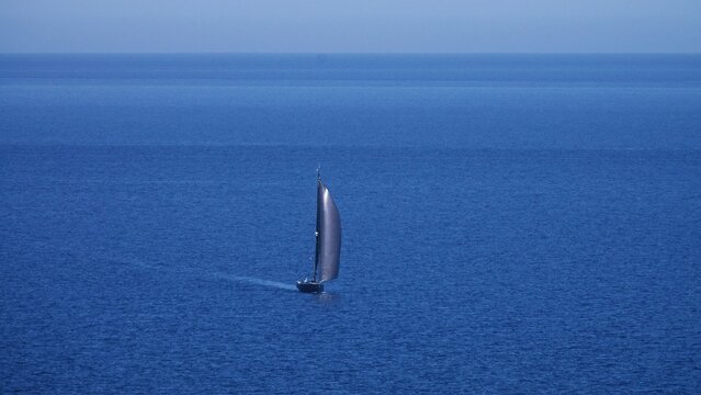 A lone sailboat navigates the expansive, tranquil waters, leaving a subtle wake behind it on a bright day
