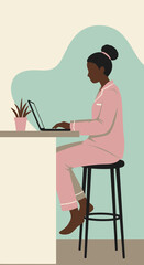 African American woman in pink pajamas working on a laptop at a home counter. Illustrates remote work, comfort, and a modern lifestyle.