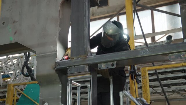 Worker in a protective mask processing a metal structure with a rotary tool
