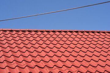 A vibrant red corrugated metal roof is visible under a power line against a clear blue sky