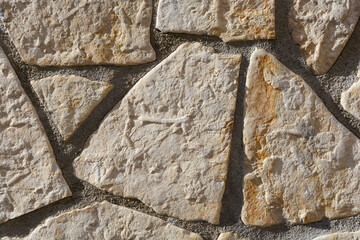 A close-up of a wall made of irregularly shaped, light-colored stones with visible mortar joints