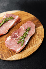 Fresh pork chops garnished with rosemary on wooden cutting board
