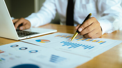 A businessman analyzes financial charts with a pen at the office desk, reviewing reports, data, and strategies for corporate success.