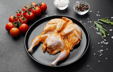 Marinated quail on black plate with tomatoes, herbs and spices on dark background
