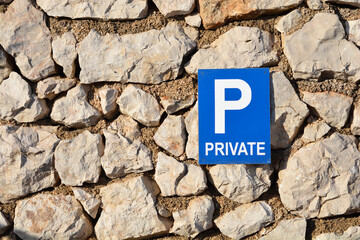 A blue and white private parking sign is mounted on a traditional stone wall, creating a contrast of man-made and natural elements
