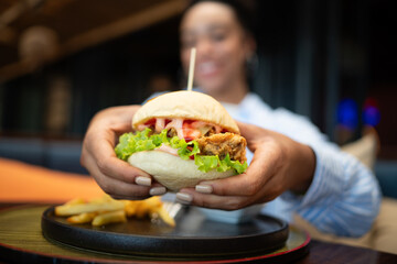 A moment of pure happiness. Smiling young woman savoring her burger and fries at a cozy restaurant