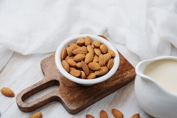 Fresh almonds in bowl near jug of almond milk on wooden board with white cloth