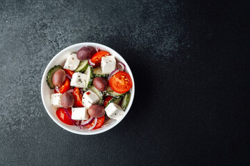 Greek salad in white bowl on dark background top view