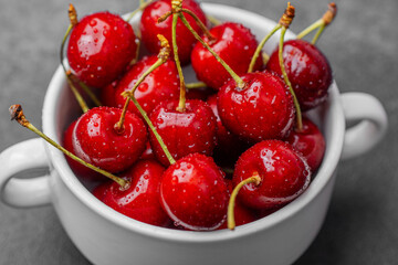 Cherries in white bowl on textured black background for seasonal fruit or rustic kitchen concept