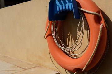 Stock photo of an orange life preserver with rope hanging on a beige wall. Safety, rescue, and...