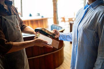 Modern hospitality, a smiling waiter accepts contactless payment from a happy customer,