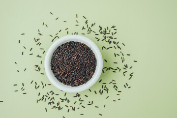Black rice in white bowl on green background with grains around