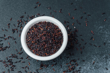 Black rice in white bowl on dark background with loose grains
