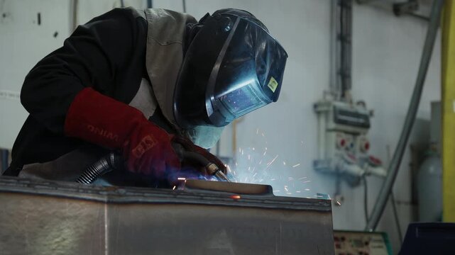 Worker in a welding mask performing welding on a metal part