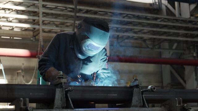 Welder in a protective mask performing welding on a metal beam