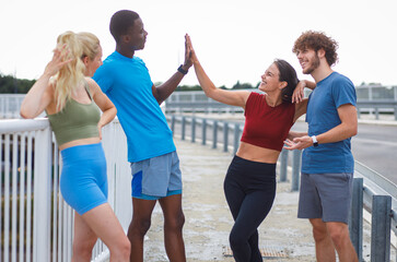 Smiling group of people are preparing for running together talking and stretching on outdoor road.