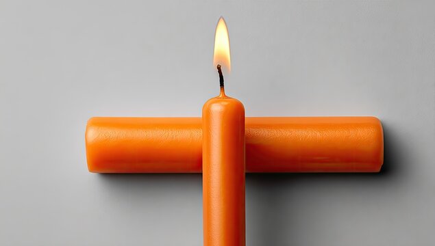 Two orange candles, one burning, on a gray surface
