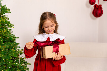 Christmas holidays concept. Happy magic little girl opens a gift box. Child is happy with a New Year's gift. The background is Christmas tree. The concept of Christmas and New Year. High quality photo