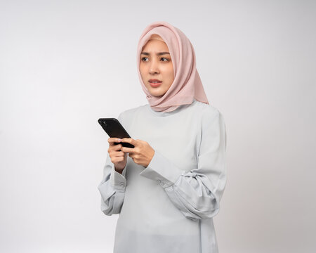 Unhappy thinking stressed young asian business muslim woman holding smartphone standing on isolated white background. Feeling stressed business Muslim woman wearing abaya and hijab fashion costume - Powered by Adobe