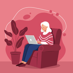 Senior woman comfortably using a laptop in her armchair at home, illustrating digital literacy and a modern, connected lifestyle.
