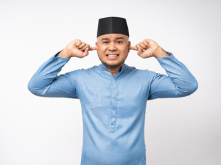 Fototapeta premium Angry boring young asian muslim man headache stressed and frustrated covering his ears with hands due to loud noise. Annoyed noise sound pollution blocking ears. Islam wearing songkok muslim costume