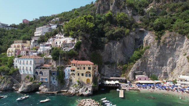 Smooth drone zoom-out revealing the colorful villas, rocky cliffs, and coastal waters of Conca dei Marini on the Amalfi Coast, starting close and pulling away for a wide scenic view.