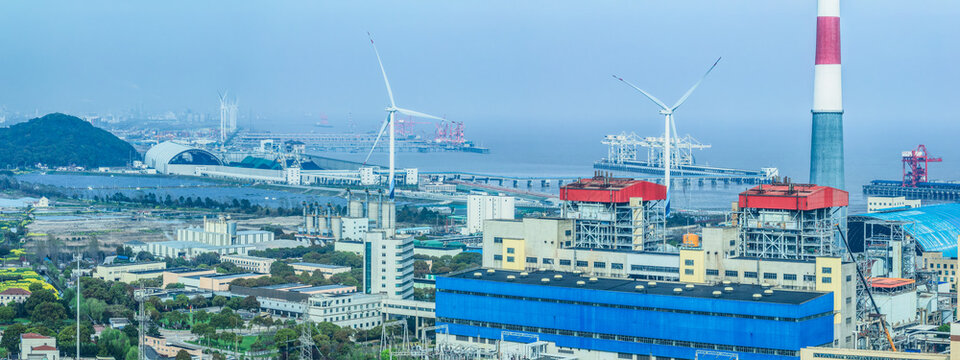 View of a modern industrial port area with power generation facilities and wind turbines on a misty day. - Powered by Adobe