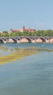 Garonne River and Pont Neuf timelapse in downtown Toulouse, France. Renaissance arch bridge reflects in the water under a blue sky with Basilica of Our Lady of the Daurade. Waterfront with green trees