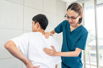 Physical therapy. Female Nurse aids young man in recovering from spine injury and providing...