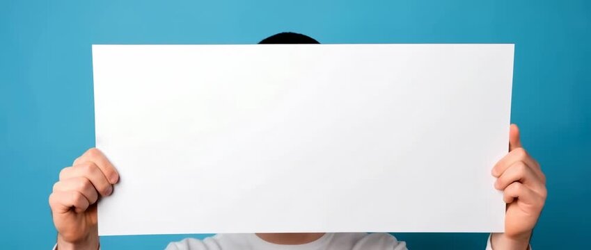 Person holding blank white poster board in front of blue background during indoor creative session at home