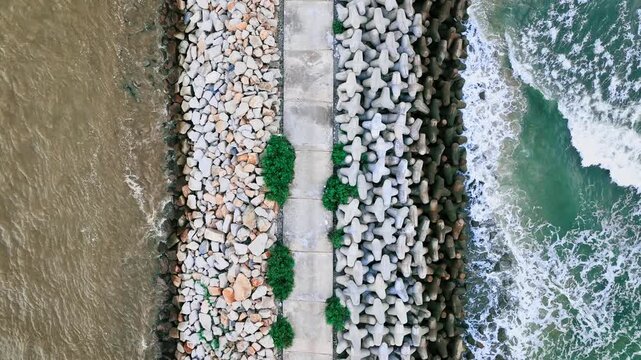 A long stone breakwater juts from the sandy shore into vast blue Loc An, creating calm shallow areas and vivid water patterns beneath a bright clear sky.