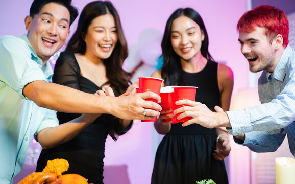 young friends raise red party cups in celebration at a fun indoor dinner party with food, laughter, and festive decorations in a colorful neon lit home