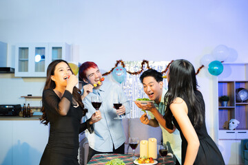 young friends feeding each other, laughing, and enjoying wine and food at a cozy indoor party with colorful decorations and a joyful vibe.