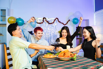 Smiling friends enjoy a delicious dinner together with wine, skewers, and salad at a cozy indoor party table, surrounded by balloons, lights, and warm celebration vibes.
