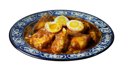 Close up of fish and egg curry dish on a decorative plate against a black background in studio lighting