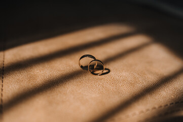 Close-up photo of wedding accessories, gold rings of newlyweds and bride in the room with shadow from sun on the floor.