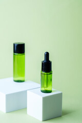 Green cosmetic dropper bottle with black cap displayed with matching container on white cube pedestal background