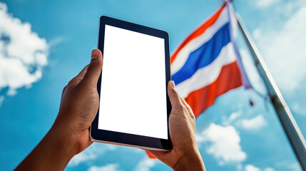 The concept of advertising a Thai mobile application or website. A mockup of a tablet in the hands of a man against the background of the flag of Thailand fluttering in the wind
