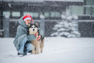 Happy girl owner wearing Santa hat hugging husky dog snowy winter