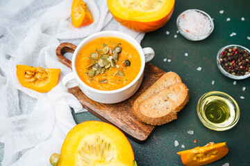 Warm pumpkin soup with seeds and bread slices on a rustic board with fresh pumpkin wedges