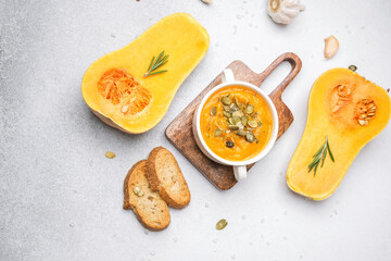 Butternut squash soup with seeds and crusty bread on a rustic board, overhead view.
